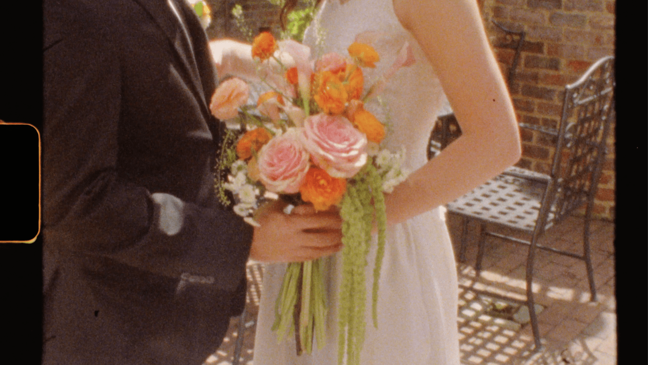 A Super8 Stillframe of Lydiq & Quinn at their Brookstown Inn Wedding in Winston Salem, a closeup on the bride's peachy orange floral bouquet
