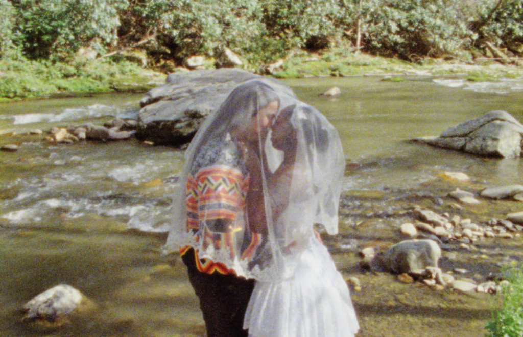 bride and groom embracing by a river in the Great Smoky Mountains with a mantilla veil draped over them; captured on Super 8 film