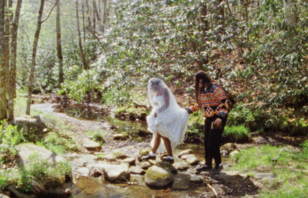bride and groom crossing stepping stones over a creek in the Great Smoky Mountains to their elopement location on Super 8mm film