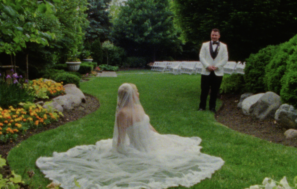 A Super 8mm Still Frame of the Bride laying down on the lush green grass of a Plainfield wedding venue garden, with the Groom watching her from afar