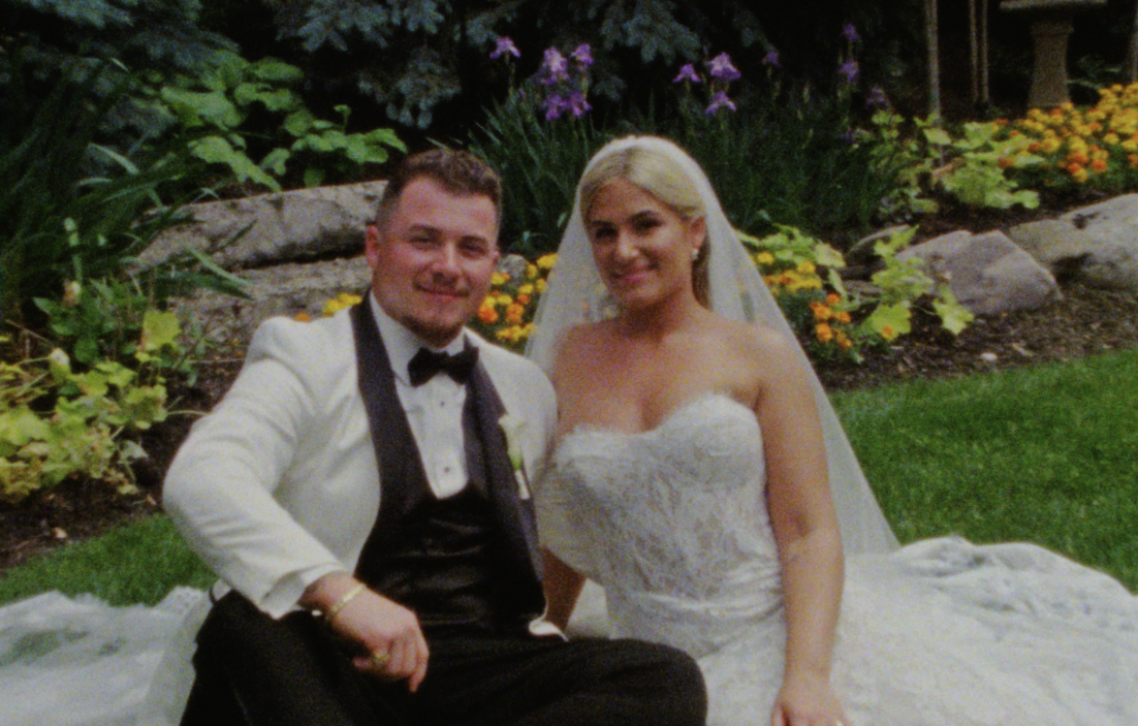 A Super 8mm still frame of the bride and groom sitting beside one another inside of a garden at the Farmhouse at Plainfield