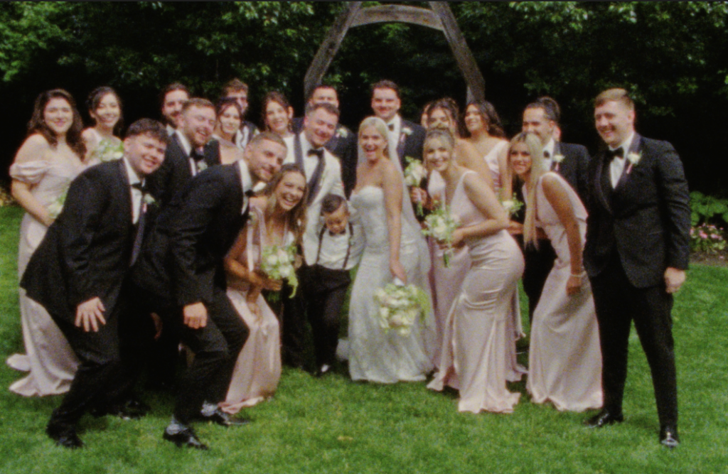 A group photo on Super 8mm film of the entire wedding party huddled together, smiling. In Plainfield, Illinois