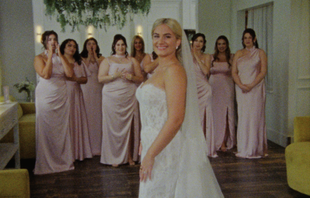 the bride posing for a portrait with her bridesmaids cheering behind her inside the farmhouse at plainfield
