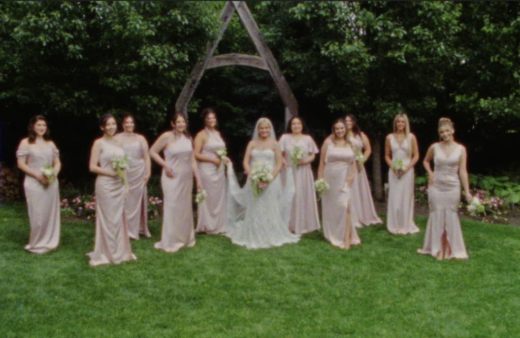 The bride and her bridesmaids in pink satin gowns posing for a portrait in the garden at the Farmhouse at Plainfield on Super 8mm film