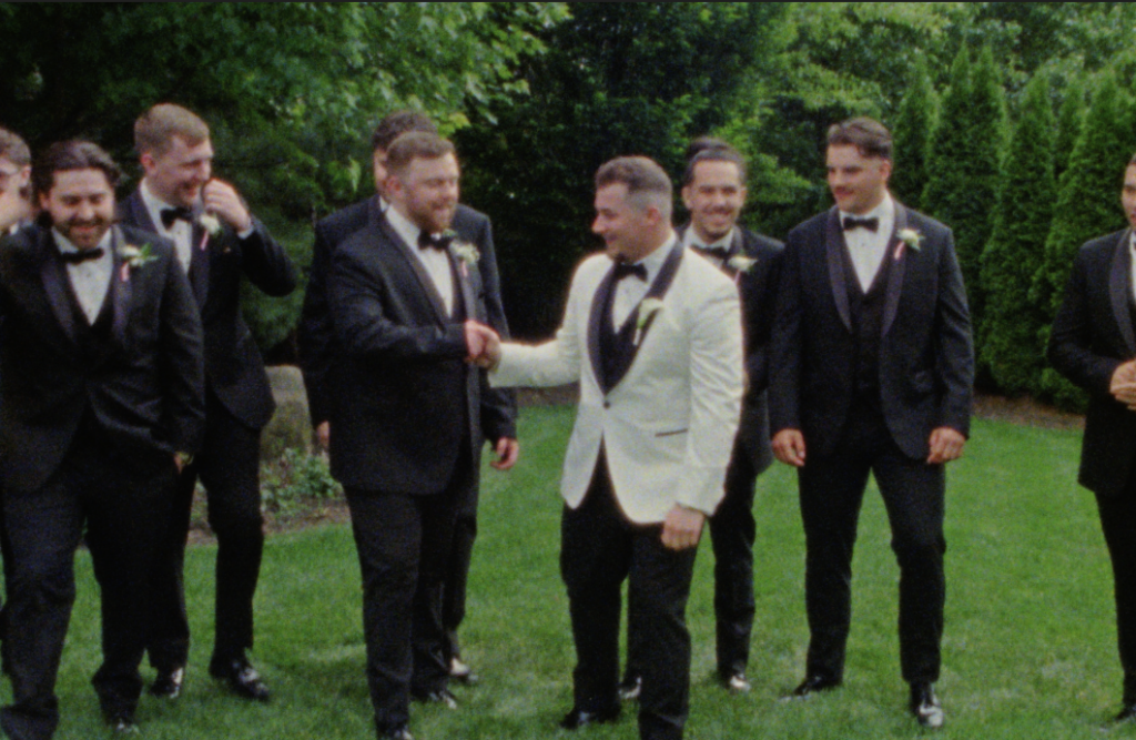 Groom fist-bumping his best man around the other groomsmen in the garden at the Farmhouse at Plainfield on Super 8mm film
