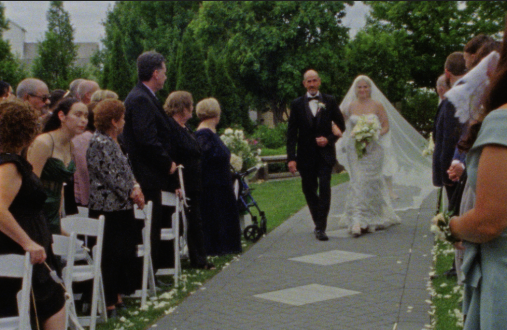 An emotional Super 8mm still frame of the bride walking down the aisle at the Farmhouse at Plainfield