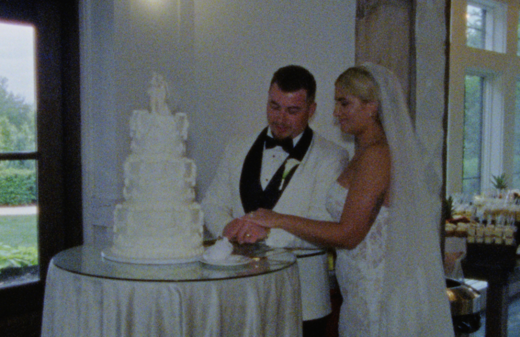 A Super 8mm still frame of the bride and groom cutting their three-tiered vintage-style wedding cake in Plainfield, Illinois