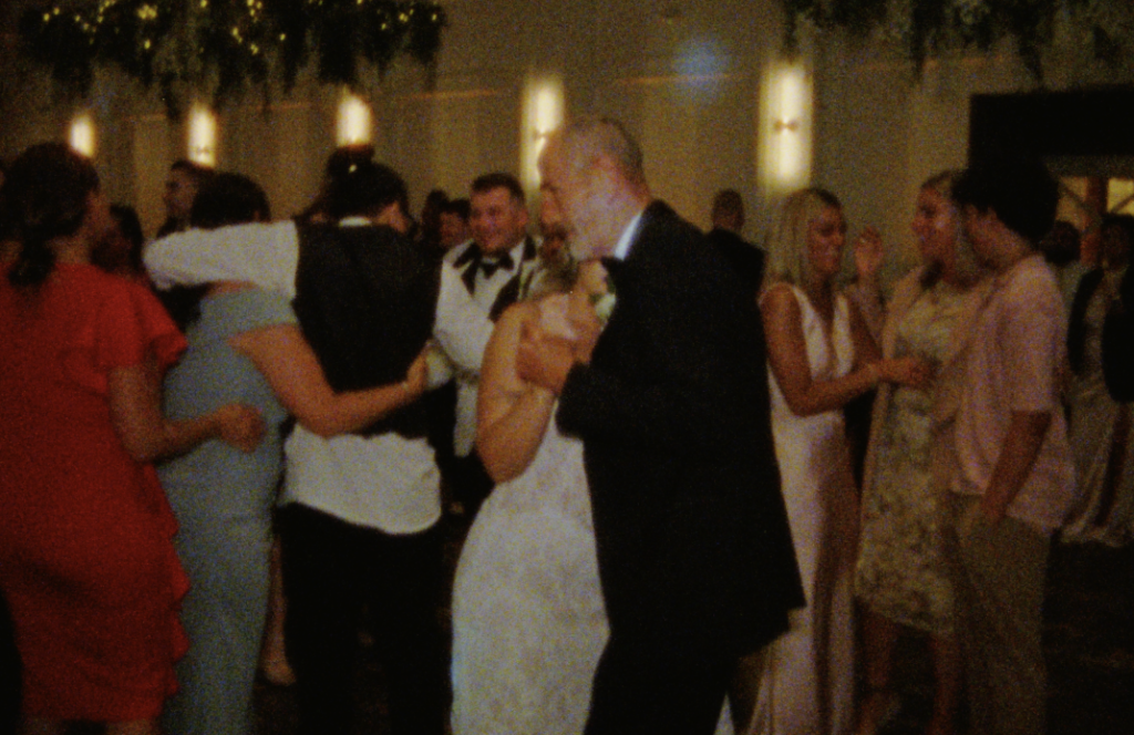 A Super 8mm still frame of the bride dancing with her loved one as the rest of the wedding guests slow dance behind them