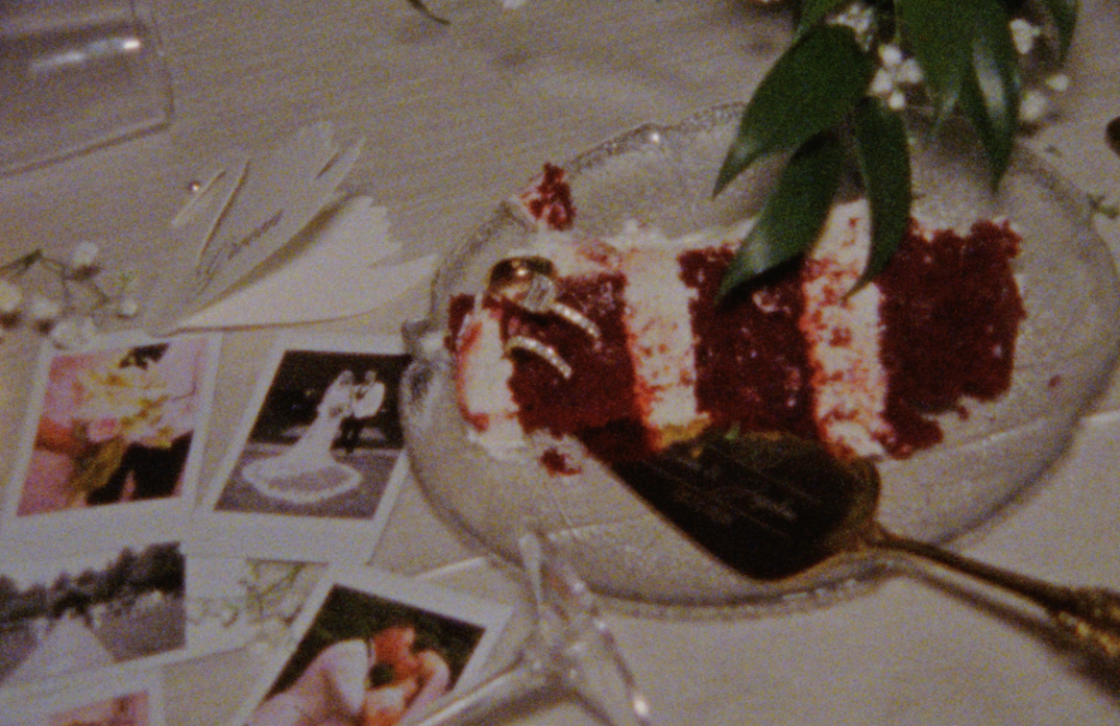A late-night Super 8mm still frame of the sweetheart's table, with polaroids spread about and a plate of red velvet cake 
