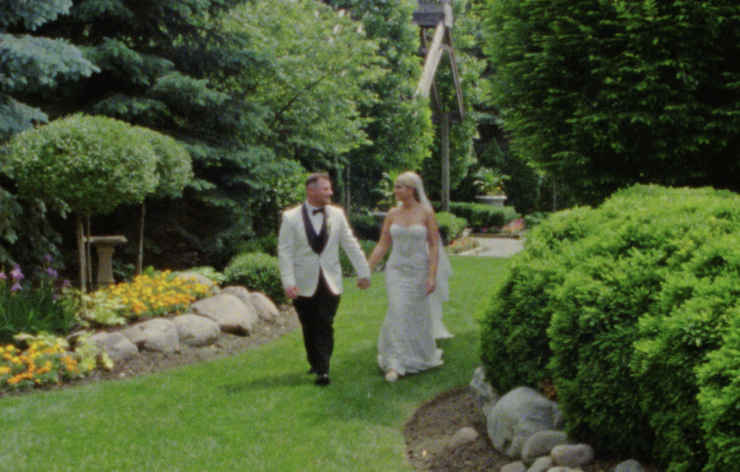 A Super 8mm Still Frame of the Bride and Groom walking hand-in-hand through a green garden at the Farmhouse at Plainfield in the greater Chicago area